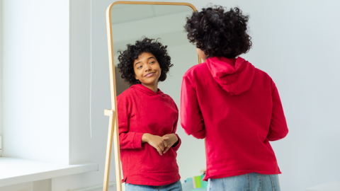 A younger woman looks in the mirror and smiles at herself.